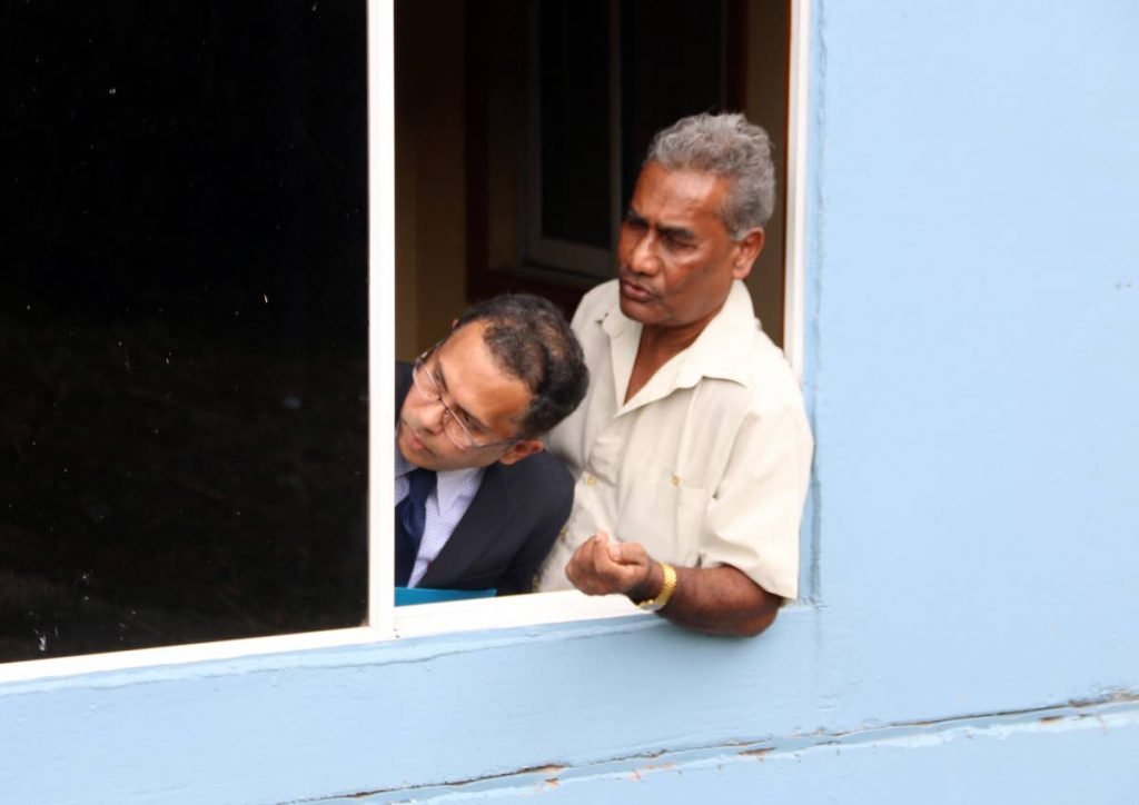 Justice Ronnie Boodoosingh, left, peers out a window yesterday as he convened court at a mandir near Princes Town which is the subject of an ongoing land dispute case.
