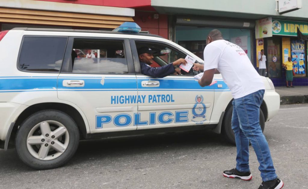 CRIME PLAN: A member of the Joint Trade Union Movement passes a flyer to police officers on High Street, San Fernando on Thursday.