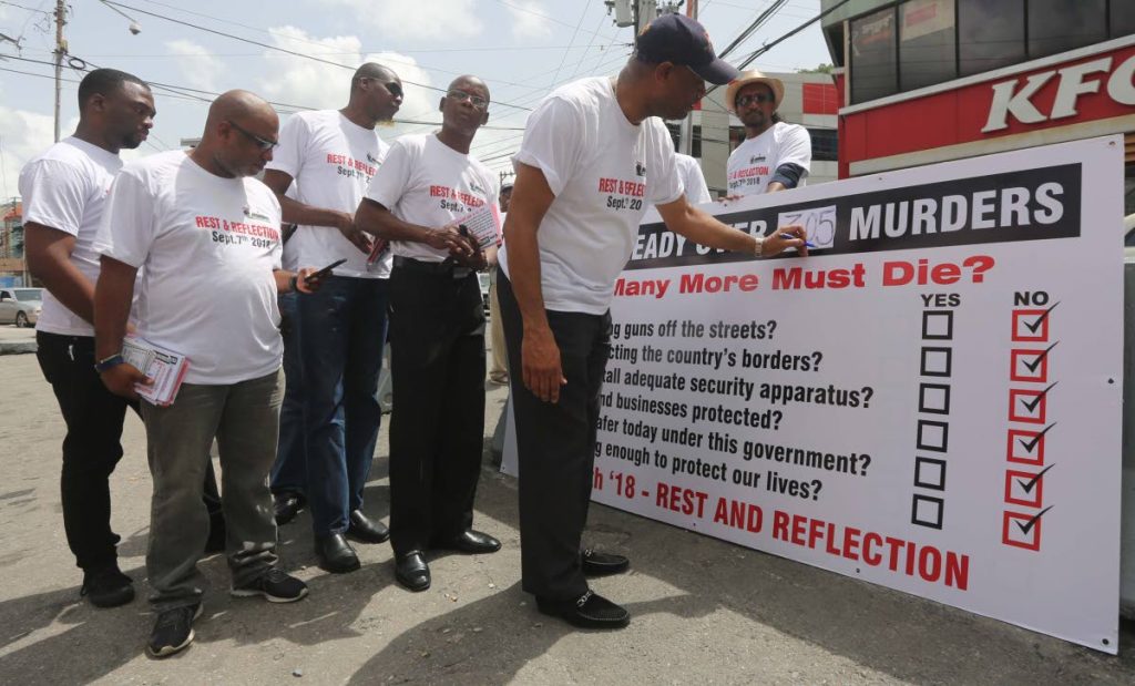 KILLING FIELDS: JTUM members looks on as OWTU President General Ansel Roget  writes 305 marking the number of murders in the country., at Library Corner, San Fernando.