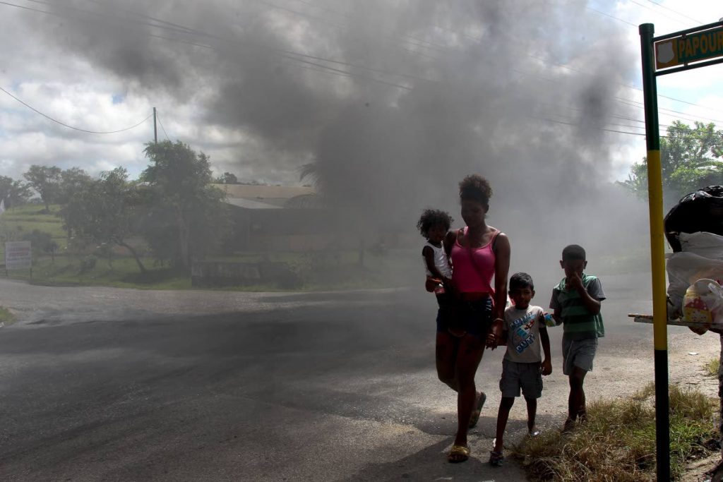 Lower Barrackpore resident, Lisa Williams and her children brave the thick smoke caused by burnt tyres and other debris residents set  on fire in protest over the bad roads in the area.
