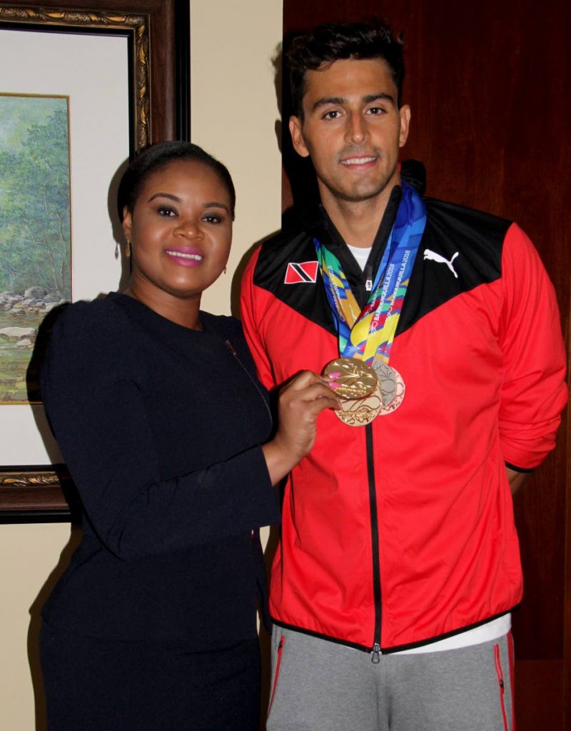 Shamfa Cudjoe, Sports Minister (left) holds one of Dylan Carter’s five medals that he earned at the CAC Games in Barranquilla, Colombia. Cudjoe met the TT swim team upon their return home at the VIP Lounge, Piarco International Airport yesterday.