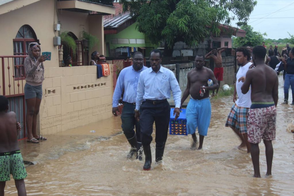 Acting Attorney General Fitzgerald Hinds and Akil Audain walk through floodwaters among residents before being kicked at with the muddy water in Beetham Gardens last Tuesday. PHOTO by ENRIQUE ASSOON
