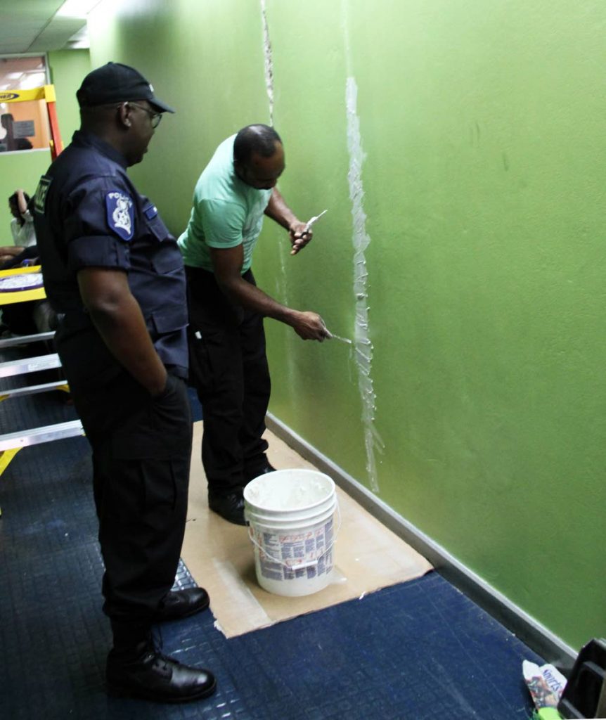 MASON COP: A policeman looks on as his colleague from the Police Service's facilities management department repairs cracks in a wall caused by Tuesday's earthquake at the Police Administration Building in Port of Spain yesterday.   PHOTO BY SUREASH CHOLAI
