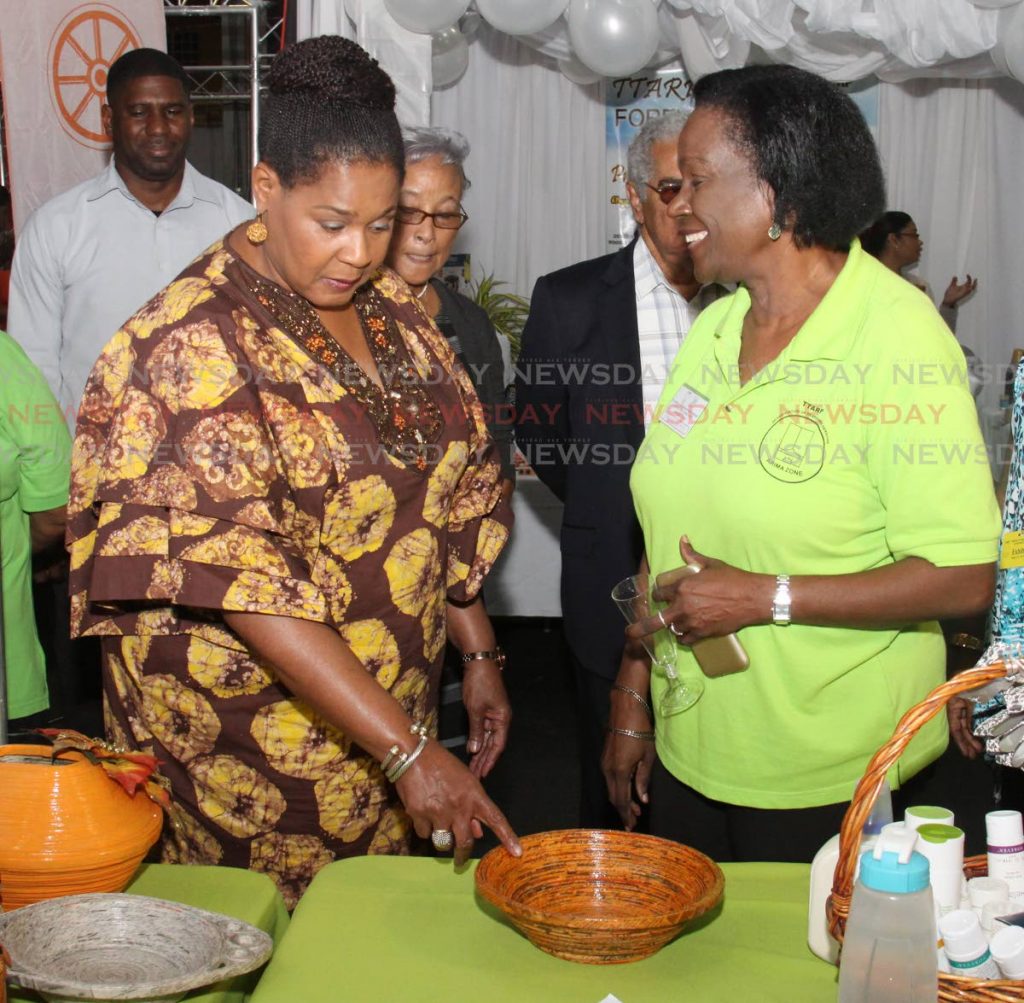 Bowled over: President Paula-Mae Weekes, left, questions Sandra Sydney, a zone representative from the Association of Responsible Persons Eastern Angels, Arima, about her paper bowl art at the TTARP 25th anniversary expo, Centre of Excellence, Macoya yesterday. PHOTO BY ANGELO  MARCELLE
