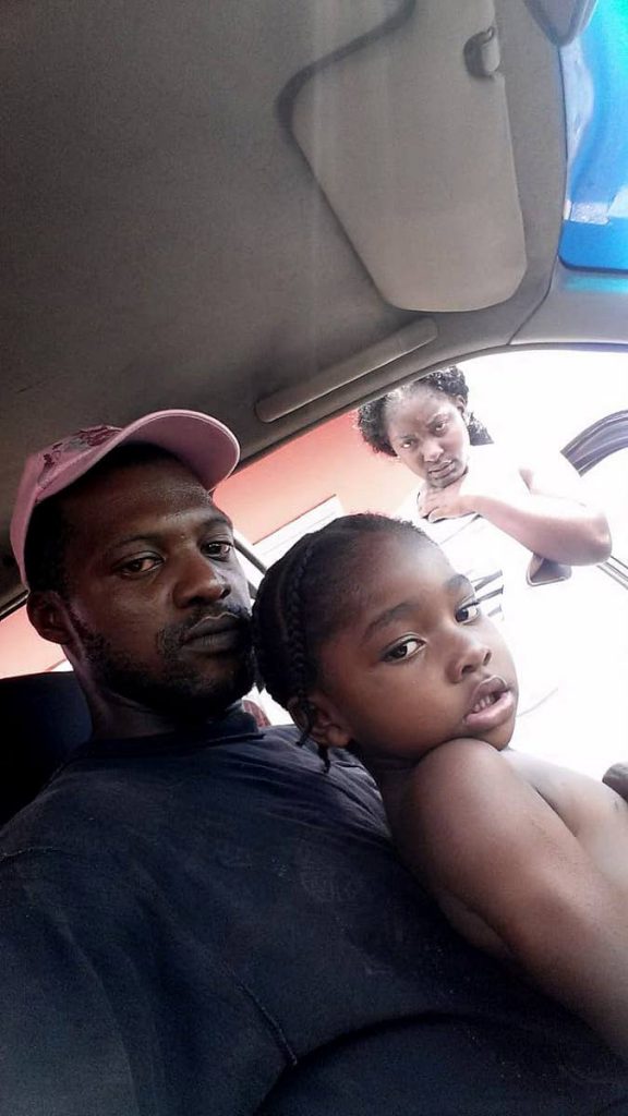 A frustrated Chinel Francis stands outside the family car, next to her husband Christopher George and their three-year-old son, Isaiah George. The couple and their four children have been living in the car. PHOTO COURTESY CHRISTOPHER GEORGE