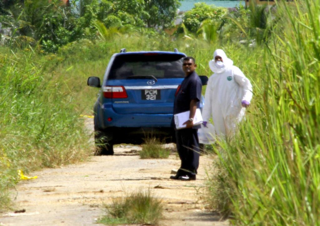 Police stand near the car in which the body of a man was found at Warren Road, Cunupia.
