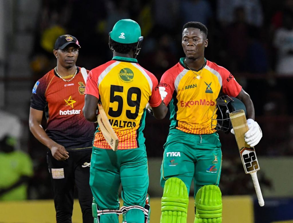 Trinbago Knight Riders captain Dwayne Bravo, left, watches as Guyana Amazon Warriors' Sherfane Rutherford, right, and Chadwick Walton celebrate victory in their final preliminary match of the Hero Caribbean Premier League at Providence Stadium, Guyana, Sunday. PHOTO BY RANDY BROOKS - CPL T20