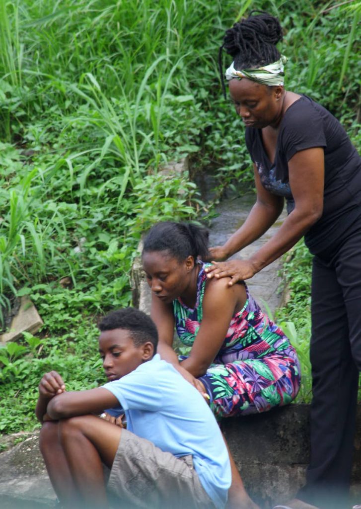 SORROW: People console each other on hearing the news that elderly siblings Victor Hutchinson, 78, and Claudette Cassell, 81, were found chopped to death yesterday in Cassell's house in Chinapoo Village, Morvant. PHOTO BY ROGER JACOB