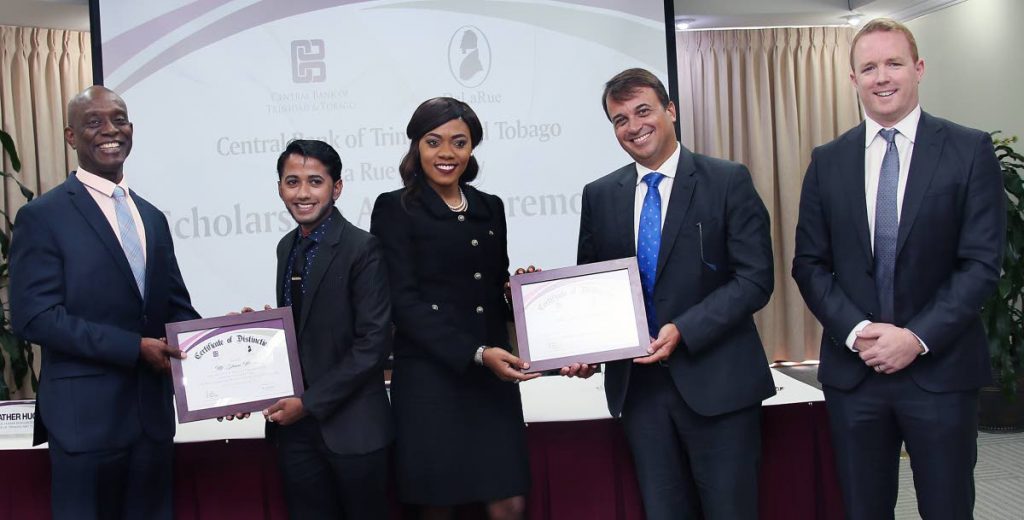 SCHOL WINNERS: Central Bank Governor Alvin Hilaire, left, presents a plaque to scholarship winner Shane Musai while De La Rue regional director and GM for Latin America and the Caribbean Fabio Ongarato, 2nd from right, presents a plaque to fellow school winner Zwena Carrington yesterday at the Central Bank in Port of Spain. At right is Gareth Evans, De La Rue currency regional manager. 
PHOTO BY AZLAN MOHAMMED