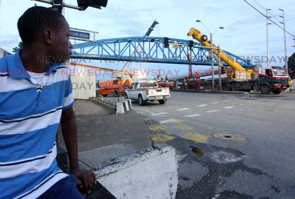 Super overpass: Carlon Haynes looks on as the Sea Lots pedestrian overpass is installated by crews over the Beetham Highway, near the Central Market, yesterday. PHOTO BY ROGER JACOB