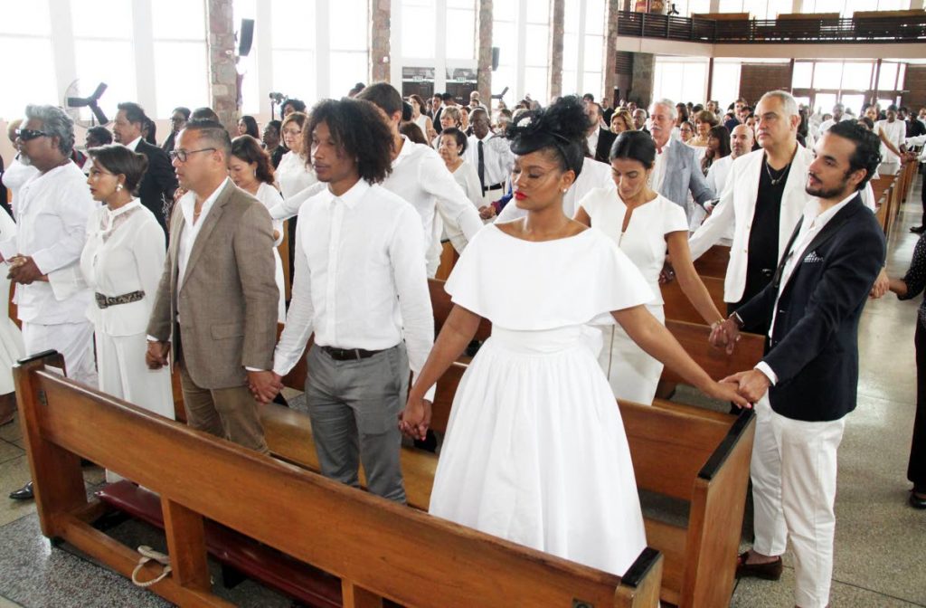 HOLD HANDS: Mourners hold hands in prayer yesterday at the funeral for fashion photographer Calvin French at the Church of the Assumption in Maraval. PHOTO BY SUREASH CHOLAI