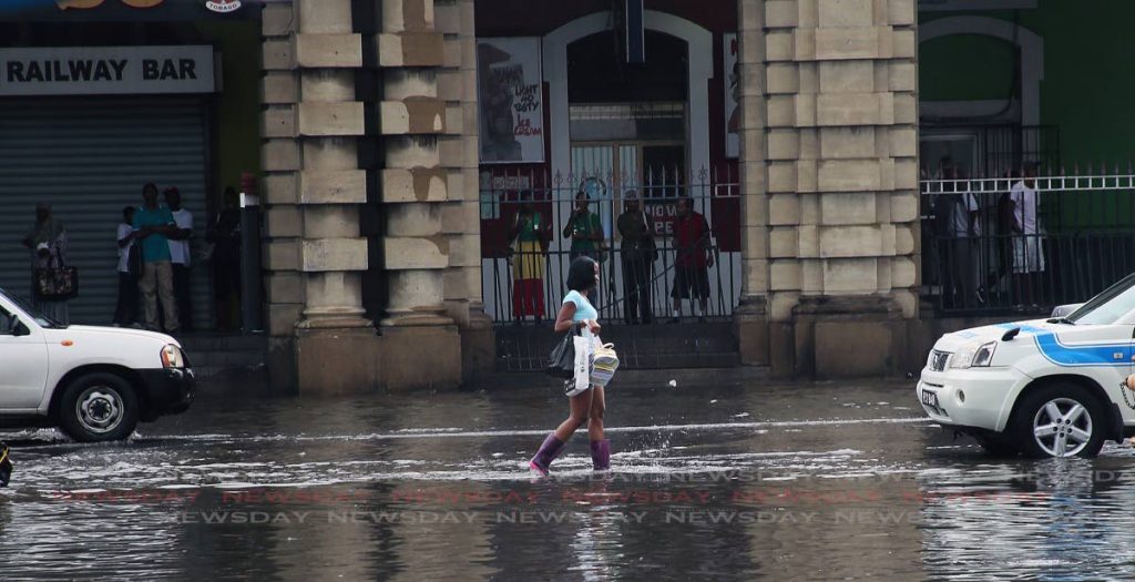 File photo: A young woman wearing a pair of boots walks along the flooded South Quay, Port of Spain, following heavy mid day rain in September 2018. 
