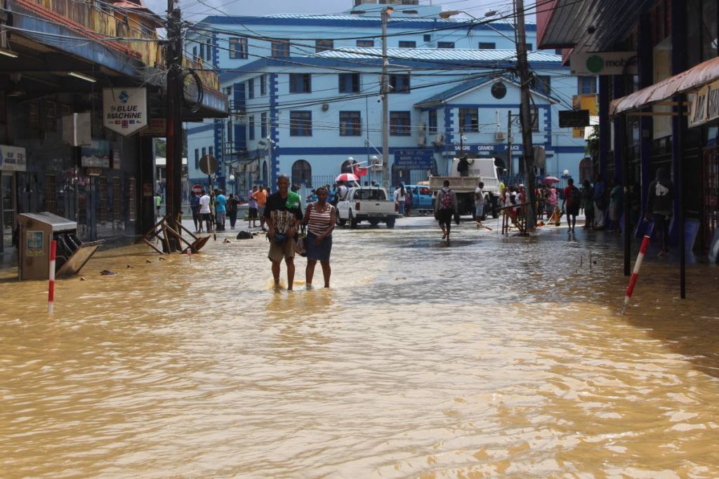 People walk along the flooded Eastern Main Road leading to the police station in Sangre Grande. PHOTO BY ENRIQUE ASSOON