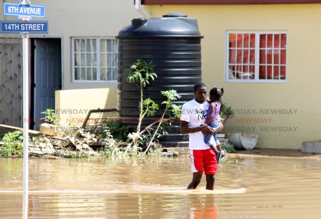 A man carries a child through floodwaters in Oropoune Gardens, Piarco on October 20. PHOTO BY ANGELO MARCELLE
