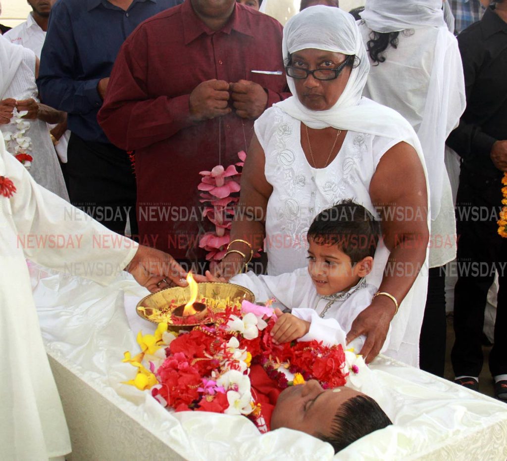 A relative helps Dylan Williams, five, to perform aarti for his father Kenwyn Williams during his funeral at Freeport yesterday. Kenwyn, a security guard, was shot and killed at a mall in Debe.

PHOTO BY ANIL RAMPERSAD. 
