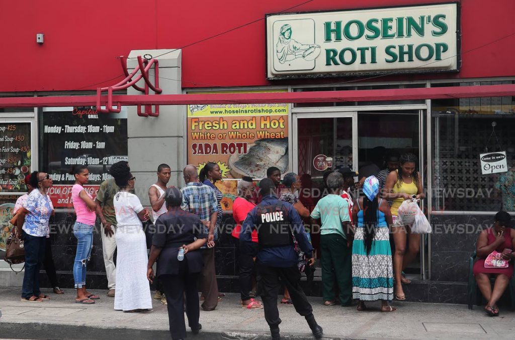 RUSH FOR ROTI: Police officers keep control of a large crowd in line to buy roti from Hosein's Roti Shop on Independence Square, Port of Spain, yesterday. Some lined up from as early at 5.30 am.
