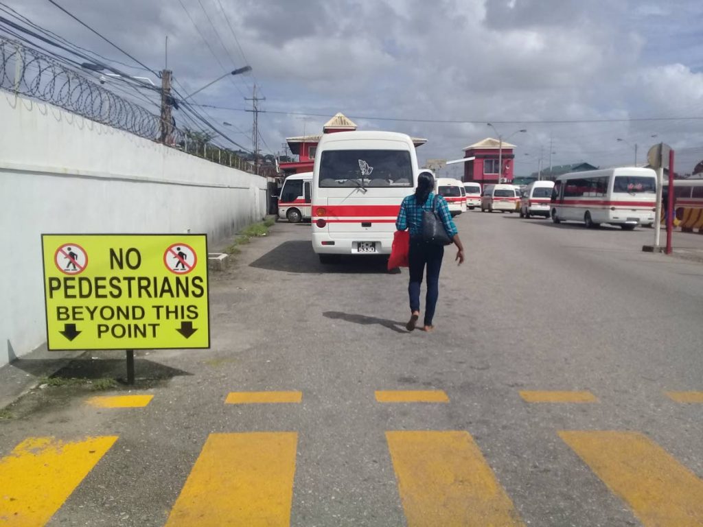 A woman walks past a sign advising pedestrian not to walk beyond the loading bay's zebra crossing at City Gate in Port of Spain. Photo by Shane Superville