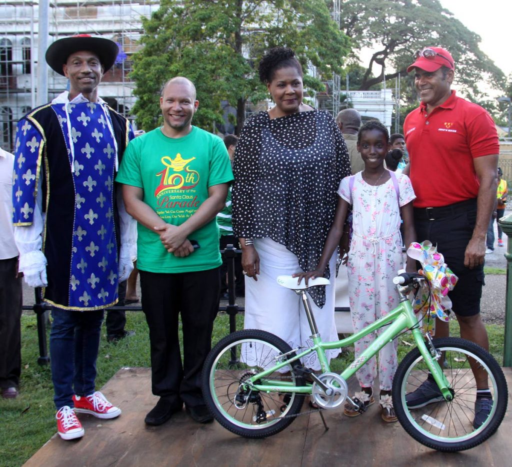President Paula-Mae Weekes, centre, with Shirmia Espinoza who received  a bicycle as a Christmas gift at the Grant-A-Wish Foundation, tenth Santa Claus Parade, Queen’s Park Savannah on Sunday afternoon. From left is Dr Curt Bodkyn, Nicholas Gordon and former national cyclist, Michael Phillips.