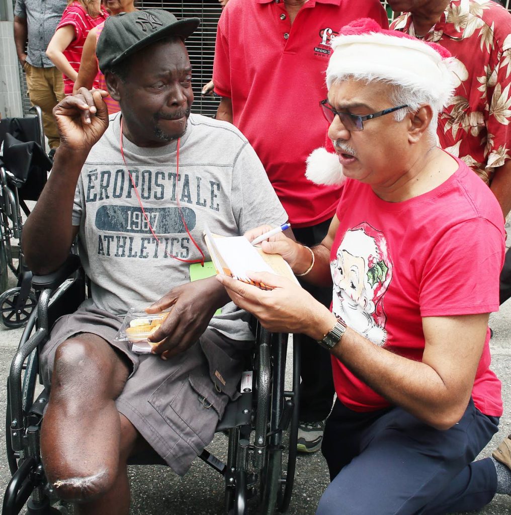 CHRISTMAS CHEER: A festive looking Minister of Health Terrence Deyalsingh takes information from wheelchair receipient  Lennox Watts after the presentation of over 100 wheelchairs by Hannah Janoura and other businesses yesterday.