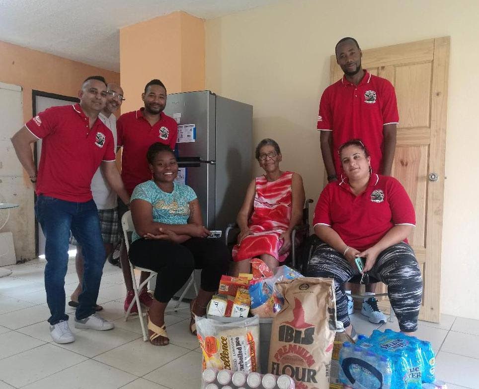 OFFERING A HELPING HAND: Greenvale resident Annette Gittens (seated at centre) with her granddaughter Shayanne (seated at left) with their array of water and food supplies, pose for a photo with Football For a Cause members Dennis Lawrence (right, standing), Nadine Khan (right, sitting), Shaun Fuentes (left), Richard Piper (second from left) and Kyle Lequay at Gittens' home on Saturday. PHOTO COURTESY TTFA.