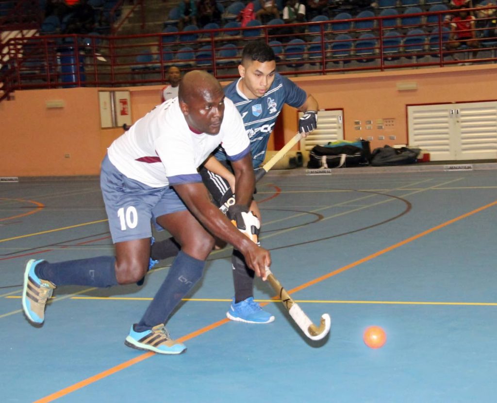 TT Defence Force's Nicholas Wren dribbles the ball as he is tracked by his Queen Park rival in the Ventures Indoor Hockey Tournament at UWI-SPEC, Friday. 
