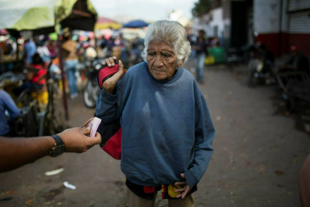HARD TIMES: An elderly woman is offered cash as she begs at a wholesale food market in Caracas, Venezuela on Monday. AP PHOTO