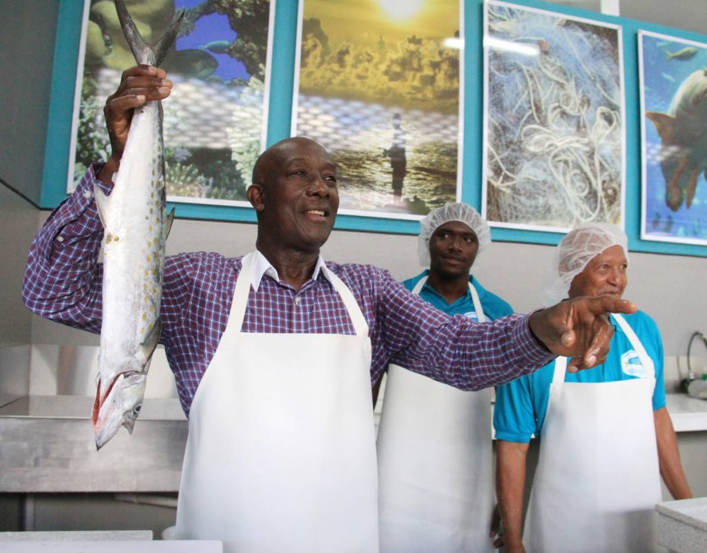 FISHERMAN: Prime Minister Dr Keith Rowley tries his hands at selling fish during the opening last year June of the Carenage Fishing Centre.