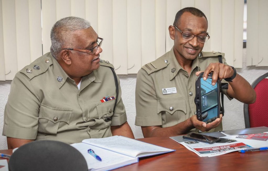 Traffic and Highway Patrol inspector Kissoon Badloo and senior superintendent Basdeo Ramdhanie examine a rear view mirror with camera which makes up part of the dashboard camera system.