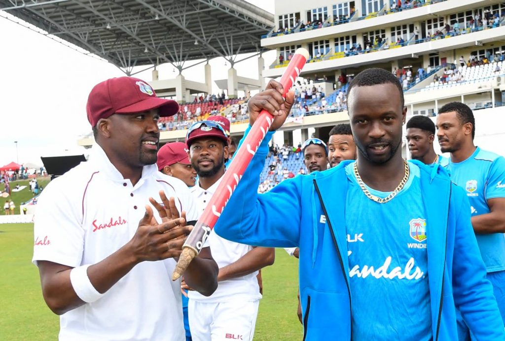 Man-of-the-Match Kemar Roach, right, and Darren Bravo, left, celebrate after West Indies thrashed England by ten wickets in the 2nd Test yesterday to win the series at the Sir Vivian Richards Stadium in Antigua. (AFP)
