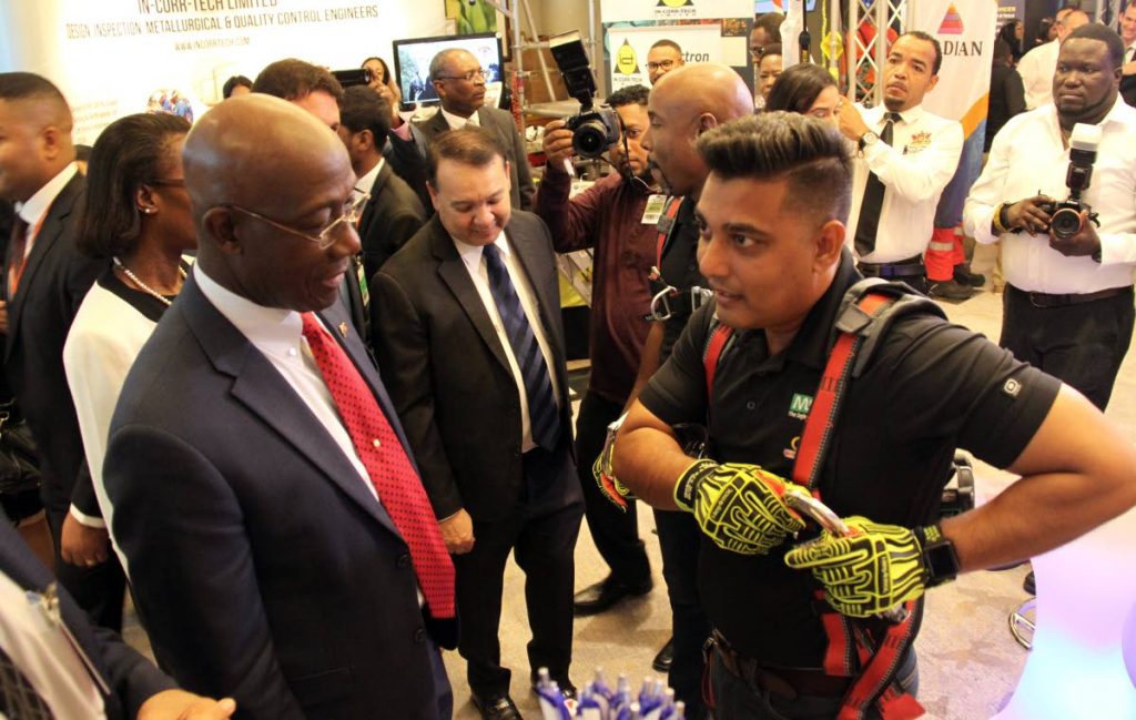 SECURE IT SO: IRP’s Fire and Safety officer Farzul Ali shows Prime Minister Dr Rowley how to secure protective gear yesterday during the Energy Conference at the Hyatt Regency in Port of Spain. PHOTO BY SUREASH CHOLAI