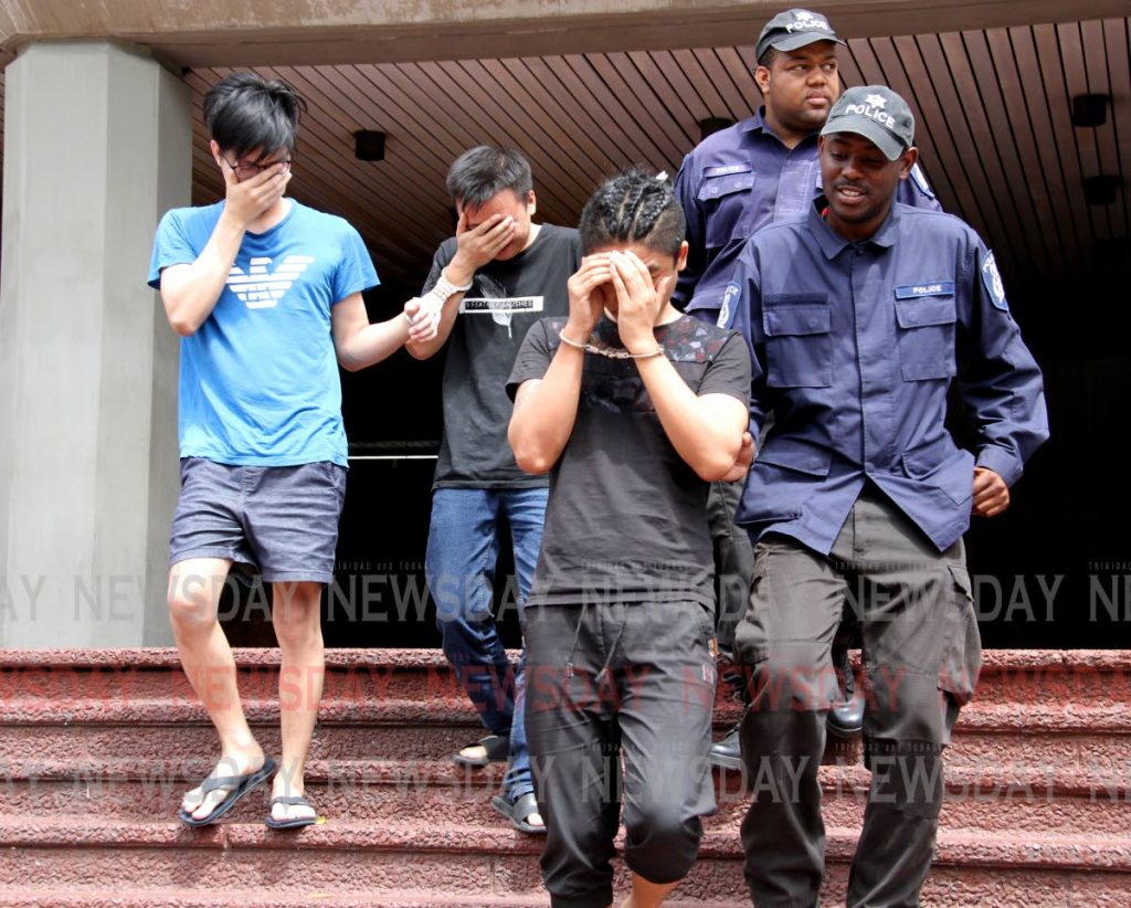 Police officers escort three Asian men out of the Hall of Justice, Port of Spain on Saturday morning after they appeared before a judge seeking release from custody as they have not been charged since their detention earlier this month. PHOTO BY SUREASH CHOLAI