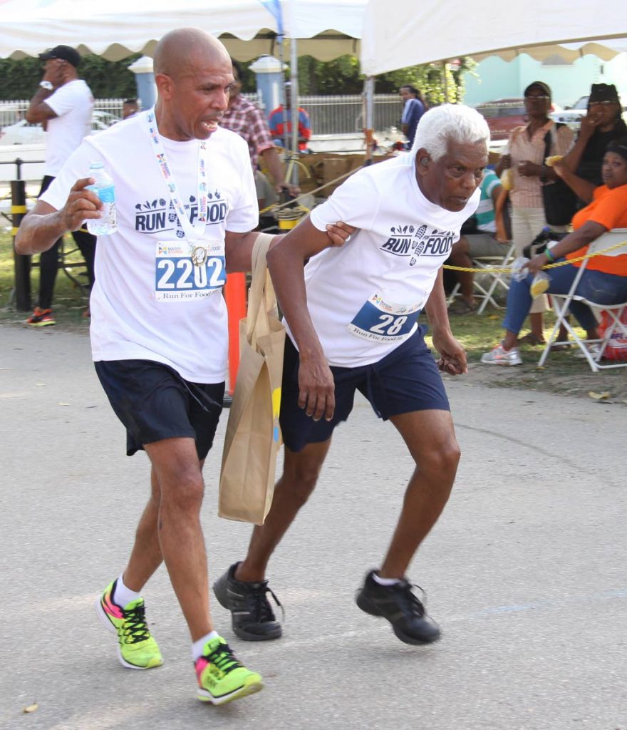 In this April 8, 2017, an elderly man is helped to the finish line at the Run for Food 5k/walk. 