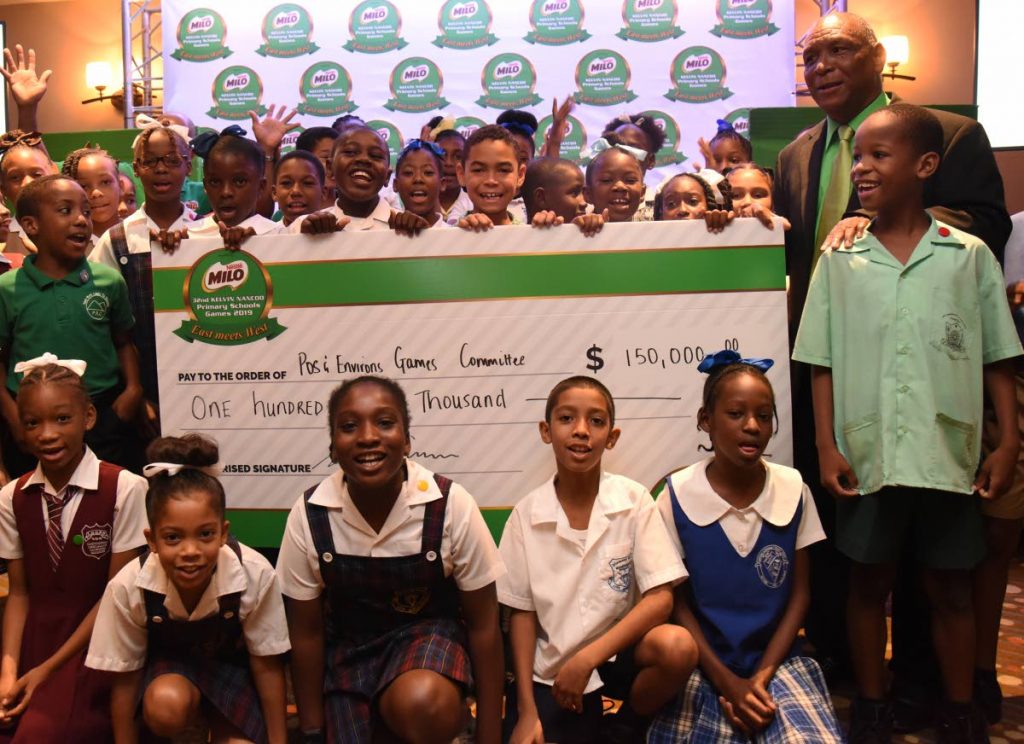 Students from various primary schools throughout the country display a cheque from sponsors of the Kelvin Nancoo Primary Schools Games, at the launch, on Tuesday. Standing at right is chair of the games Mr Kelvin Nancoo.