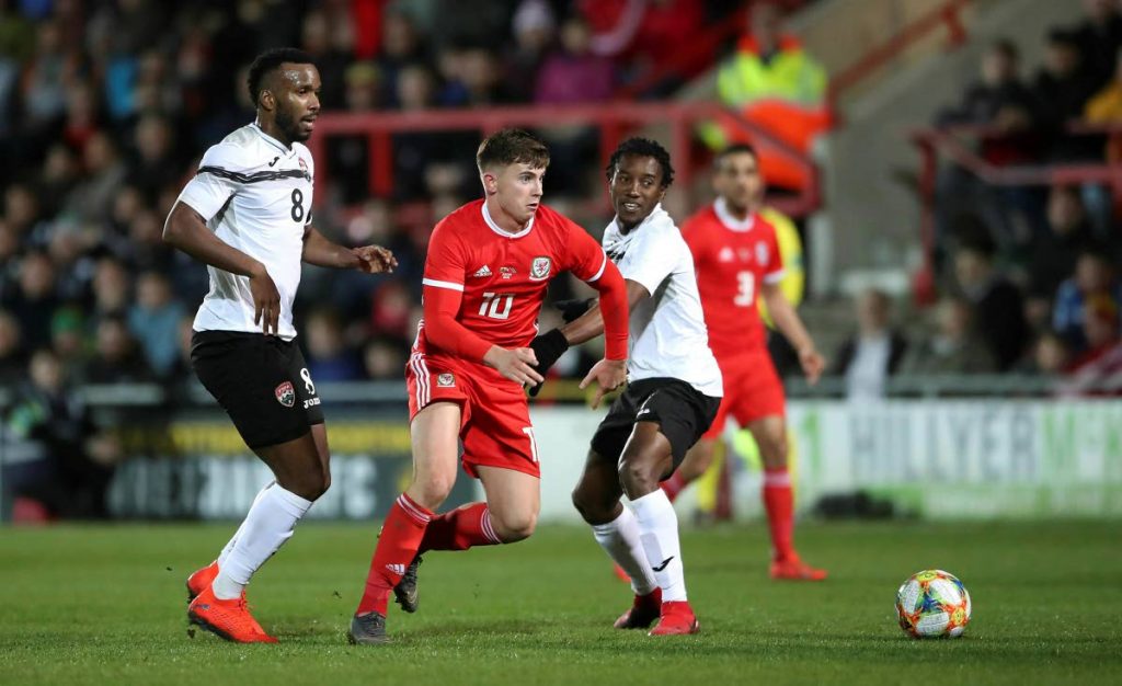 TT’s Khaleem Hyland, left  and Wales’ Ben Woodburn, centre, vie for the ball  during the international friendly, at the Racecourse Ground, in Wrexham, Wales, on Wednesday. Wales won 1-0. (via AP)