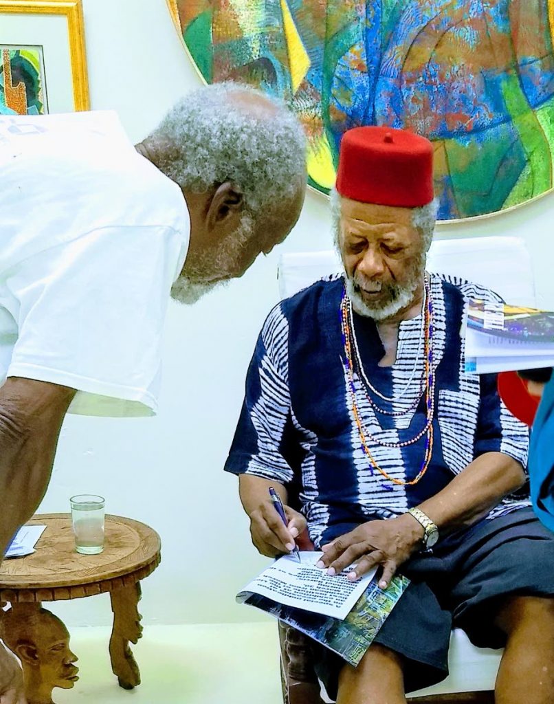 Artist LeRoy Clarke signs a commemorative copy of the T&T Review at the art show launch on March 19 at the Lloyd Best Institute of the Caribbean in Tunapuna.