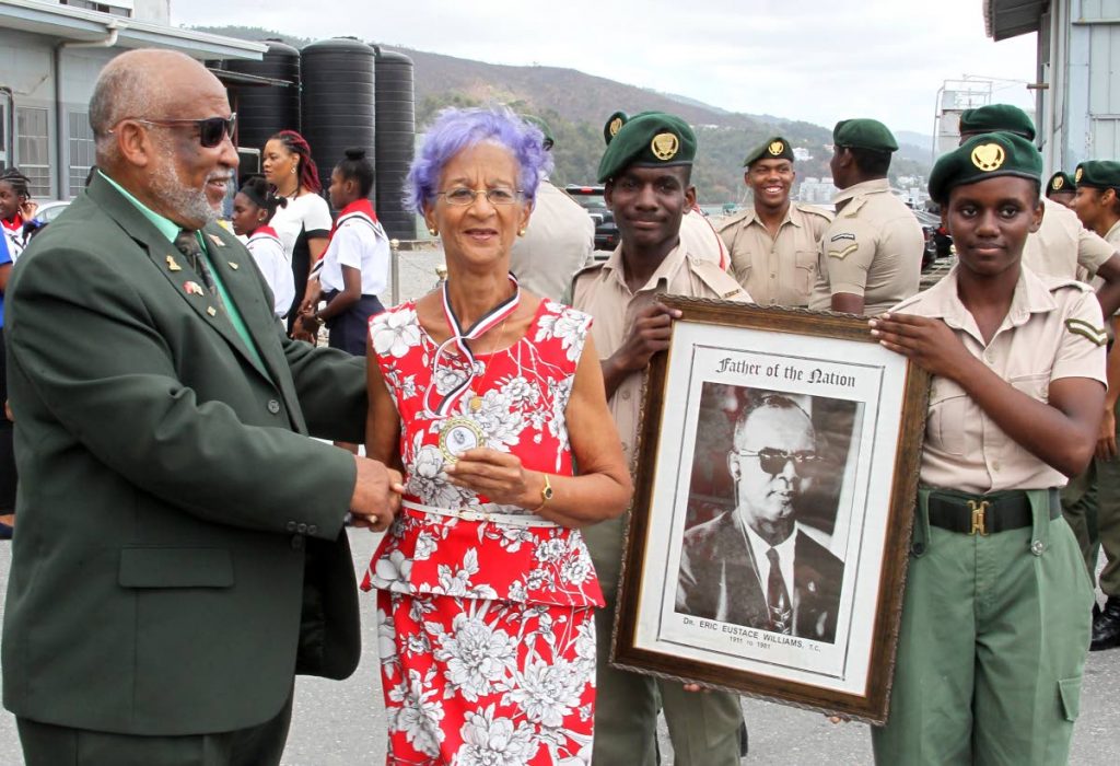 Patricia Gittens, niece of Dr Eric Williams, accepts the Father of the Nation medal of honour from chairman of the Dr Eric Williams Memorial Committee Reginald Vidale as cadets hold a portrait of TT’s first prime minister during a ceremony to commemorate the 38th anniversary of his death at the heliport, Chaguaramas yesterday. PHOTO BY ROGER JACOB