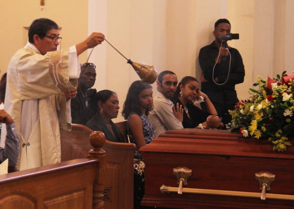 Deacon Derek Walcott burns insence during the funeral of late cuatroist Robert Munro at the Rosary RC Church, Henry Street, Port-of-Spain yesterday. Also in the photo is his daughter Maria Elena Newallo-Munro who is being comforted by her cousin Shane Newallo. PHOTO BY AYANNA KINSALE