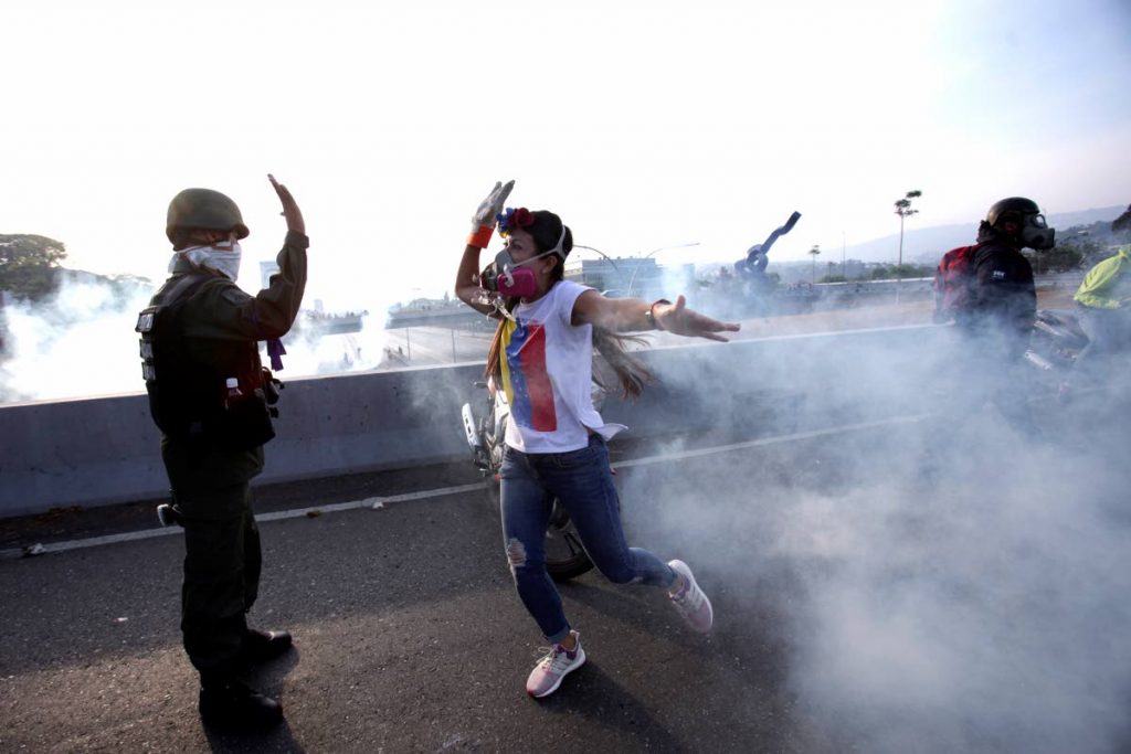 An opponent to Venezuela's President Nicolas Maduro high fives a rebel soldier on a highway overpass outside La Carlota air base amid tear gas fired by loyalist soldiers inside the base in Caracas, Venezuela, Tuesday, April 30, 2019. Venezuelan opposition leader Juan Guaidó took to the streets in Caracas with activist Leopoldo Lopez and a small contingent of heavily armed troops early Tuesday in a bold and risky call for the military to rise up and oust socialist leader Nicolas Maduro. (AP Photo/Boris Vergara)