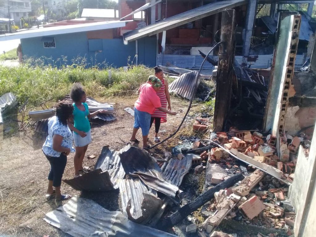 Two of the homeless people and other relatives  look at the burnt ruins of the house fire at Princes Town.