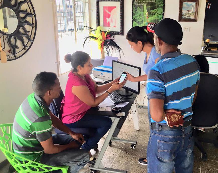 Andreina Briceno-Brown, second from left, helps a Venezuelan to access information online about registering at La Casita House, Arima. Photo courtesy Andreina Briceno-Brown