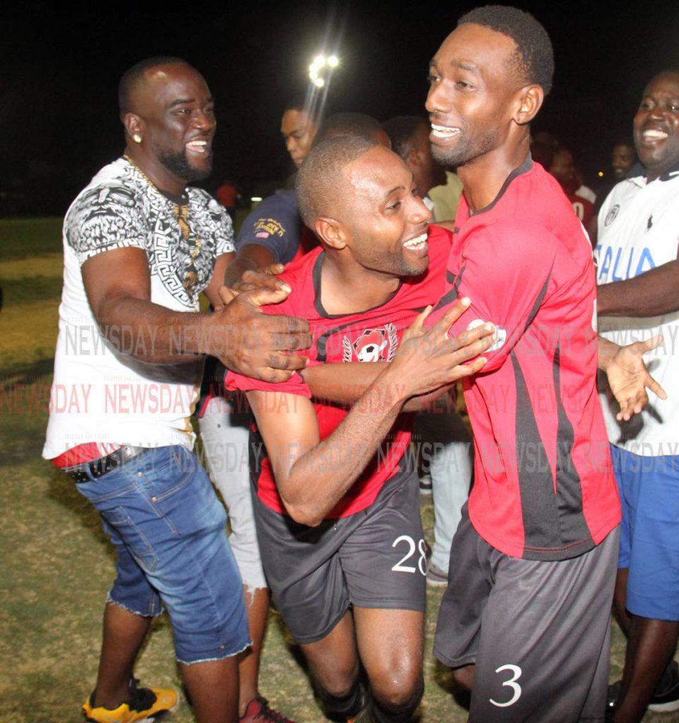 Boys Town Strikers' Irvin Reyes, centre, is mobbed by teammates and supporters after scoring the decisive penalty in the Sweet Sixteen final against Athletico at the Ojoe Road Recreation Ground, Sangre Grande. PHOTO BY ANGELO MARCELLE 