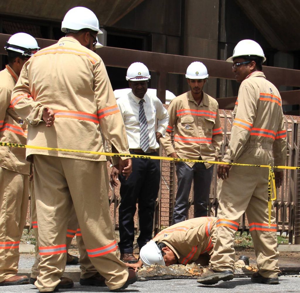 HAVING A LOOK SEE: In this file photo T&TEC general manager Kelvin Ramsook (kneeling) examines buried cables under the pavement outside 
the Hall of Justice which was the scene of the explosion. PHOTO BY AYANNA KINSALE 