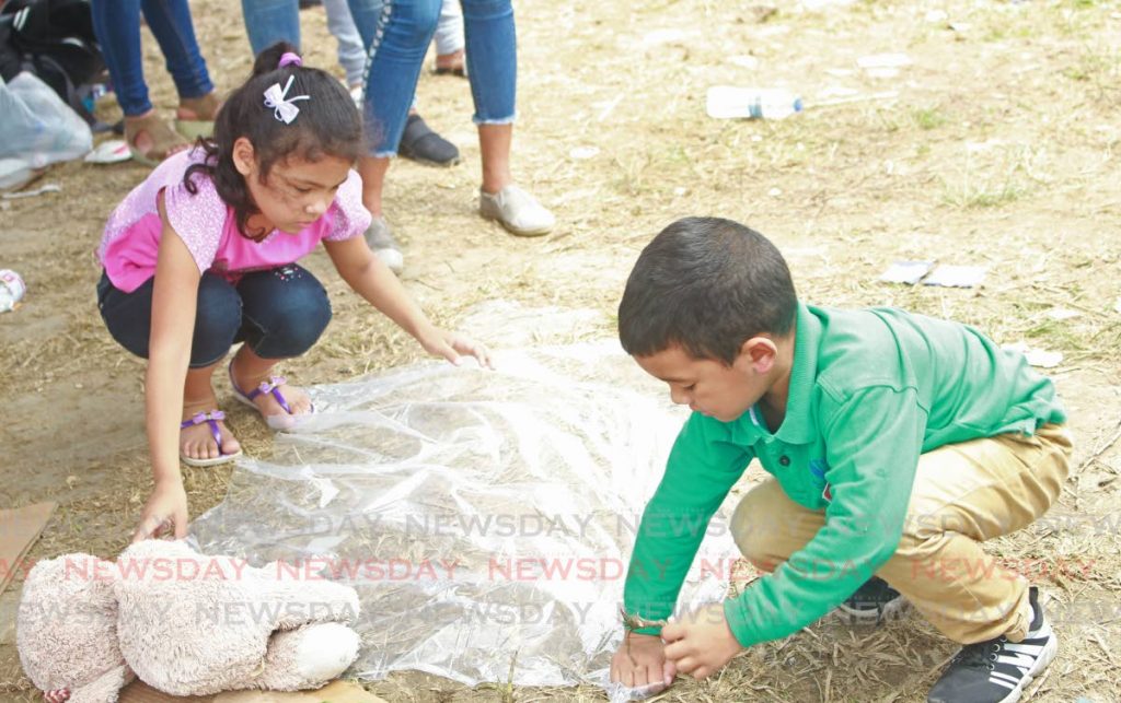Venezuelan children spread plastic to rest on while their relatives register at Achievors Banquet Hall, Duncan Village, SAn Fernando yesterday. PHOTO BY CHEQUANA WHEELER