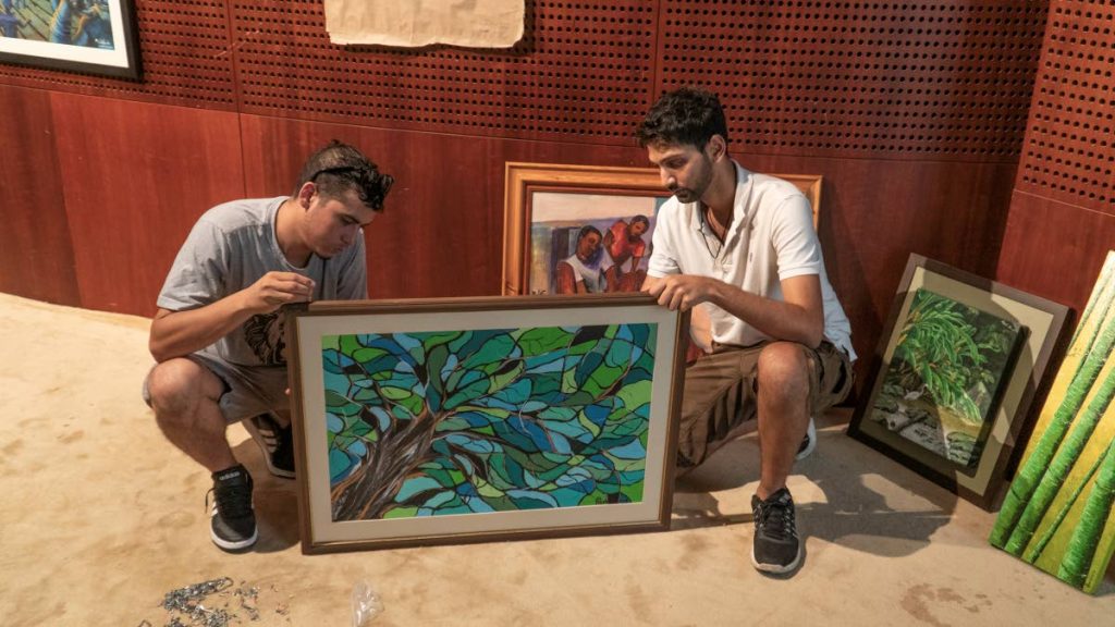 Visualart Galleries directors Jonathon Mora, left, and Joshua Persad, get Nicole Tang's painting Looking Up From Under The Tree ready to mount up for the exhibition.