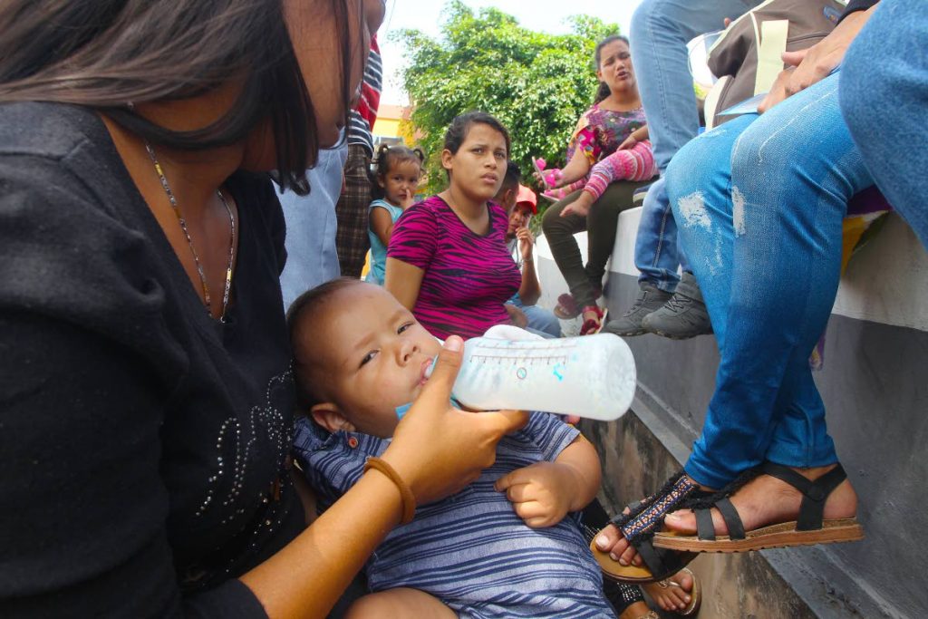 ROADSIDE FEED: Baby boy Haiseell Caraballo drinks from a bottle as he and his mother joined hundreds of Venezuelans in line waiting to be registered yesterday at the Achievors Banquet Hall in San Fernando. PHOTO BY LINCOLN HOLDER