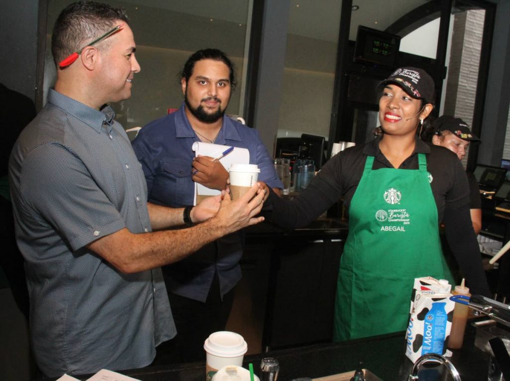 Starbucks Barista Competition: Munroe Road Starbucks employee, Abegail Boodram, serves competition judge and Starbucks Washington DC district manager Jose Castro, her final competition drink. The event was held at Starbucks Trincity Plaza. Also in photo is 2018 Barista Champion and judge, Bradley Gras.