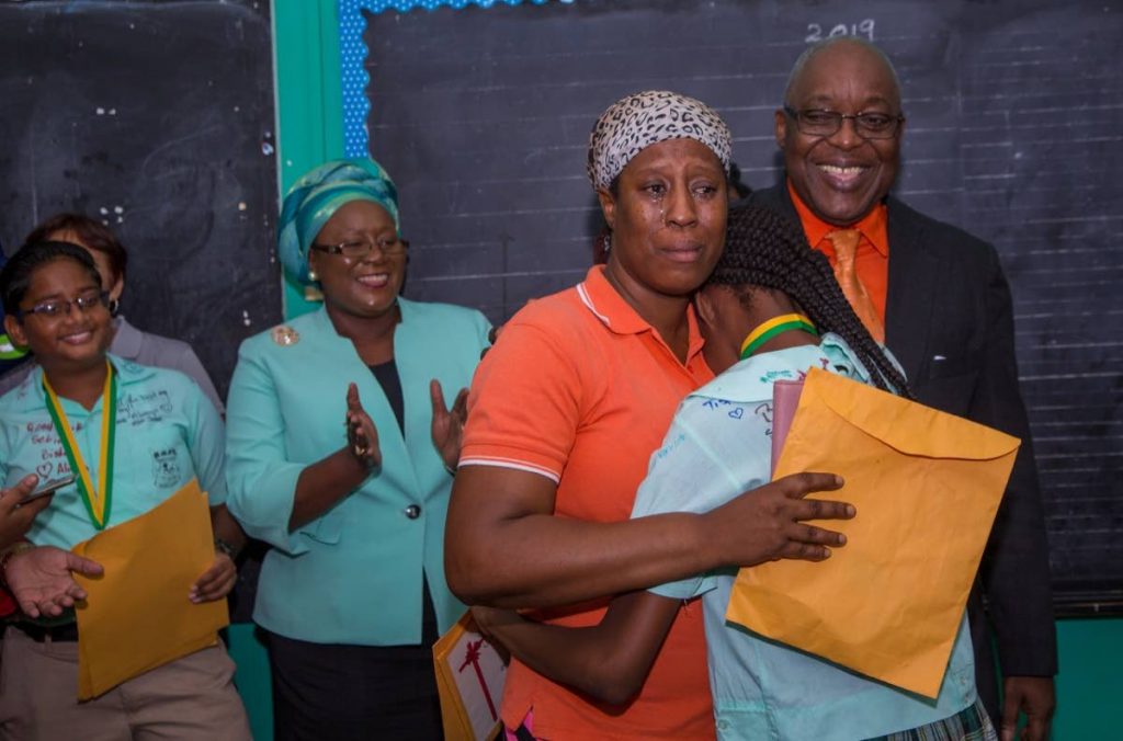 Buccoo Government Primary School student Adana Rodriguez, right, hugs her mother Dianna Rogers after receiving her SEA results on Friday. THA Chief Secretary Kelvin Charles smiles in the background as other school officials and students applaud. PHOTO BY DAVID REID