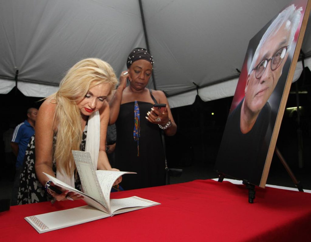 Cecilia Salazar, signs the condolence book at the wake for slain actor Raymond Choo Kong at the Arima Boys RC Primary School Penelope Spencer looks on.