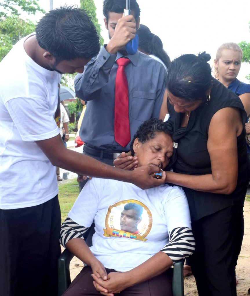 OUT COLD: A relative places a bottle of smelling salts to the nose of Samoo Ali who fainted yesterday during the cremation of her murdered son, fisherman Anand Rampersad at the Waterloo cremation site.