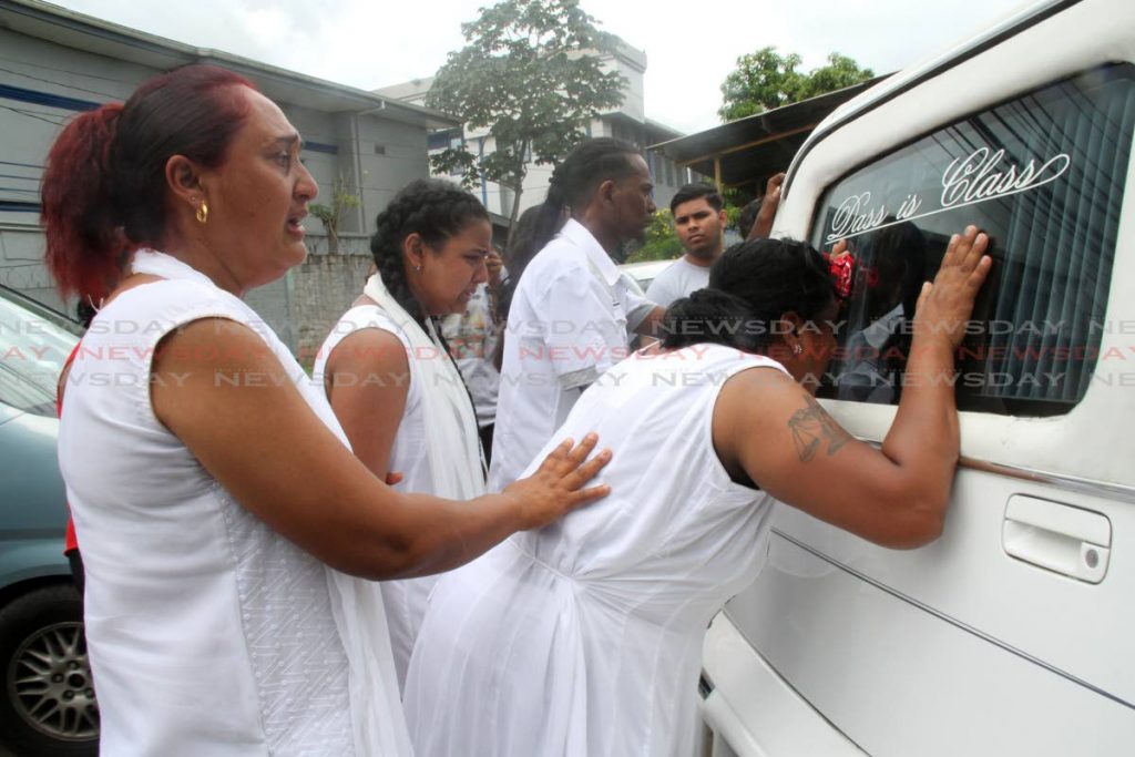 Consoled by relatives , Runa Kissoon mother of dead fisherman Brandon Kissoon rests her head on the hearse carrying her son as it leaves their home. Photo by Vashti Singh